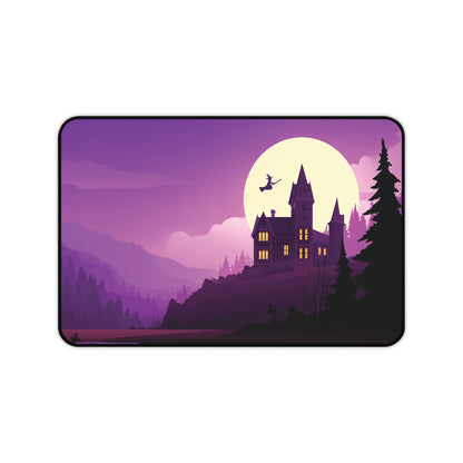 A rectangular desk mat with rounded corners featuring a stylized purple and black illustration of a haunted house on a hill under a large pale moon, with a witch flying on a broomstick.