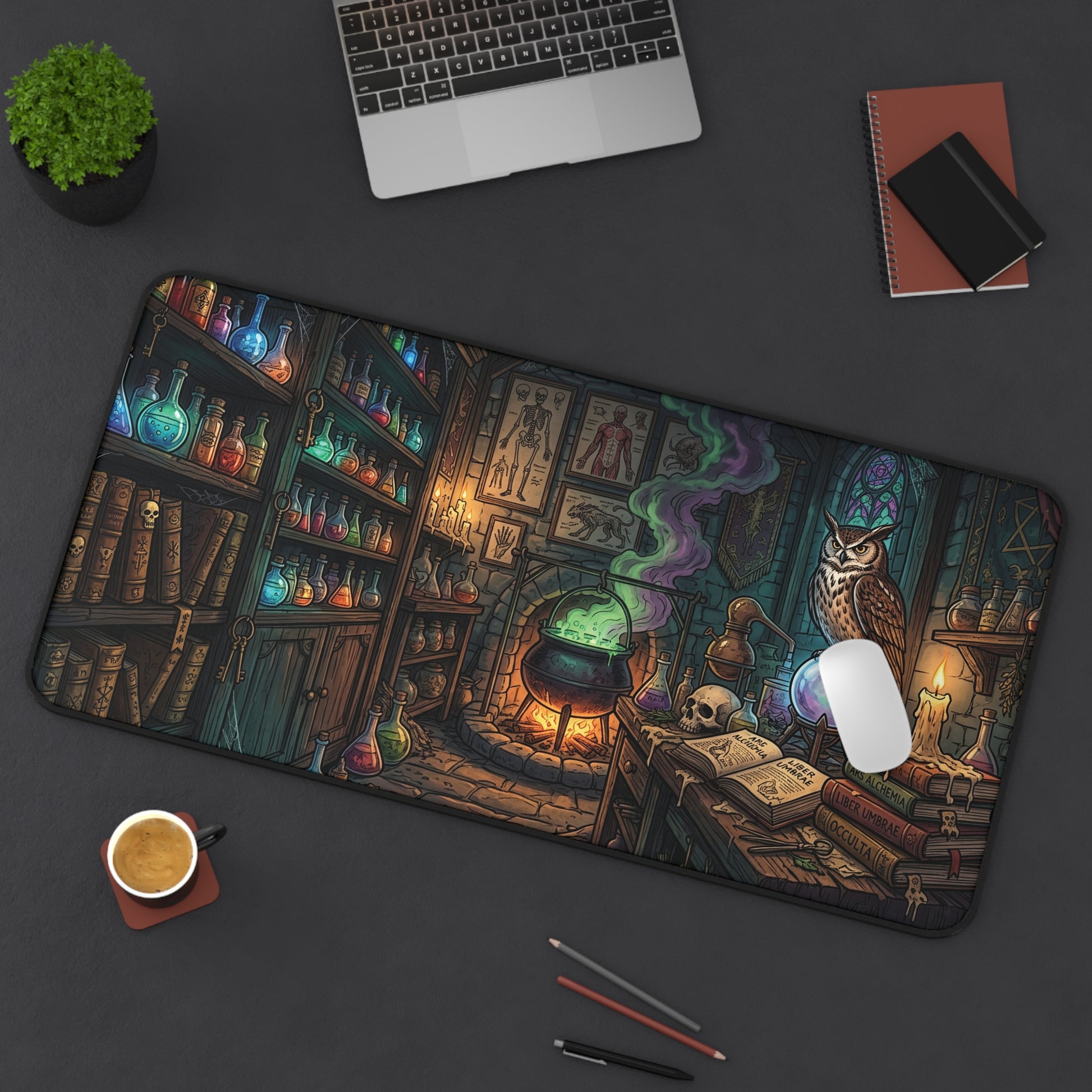 A large rectangular desk mat with a detailed fantasy illustration of a witch's library, shown on a dark gray desk with a laptop, coffee cup, and notebooks around it. The mat features an owl, cauldron, books, and glowing potions.