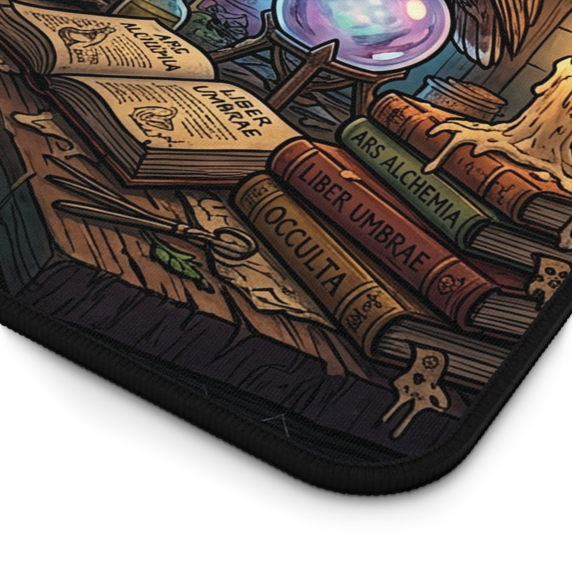 A close-up of a black-edged mouse pad featuring a detailed fantasy illustration of occult books, a crystal ball, and magical tools on a wooden surface.
